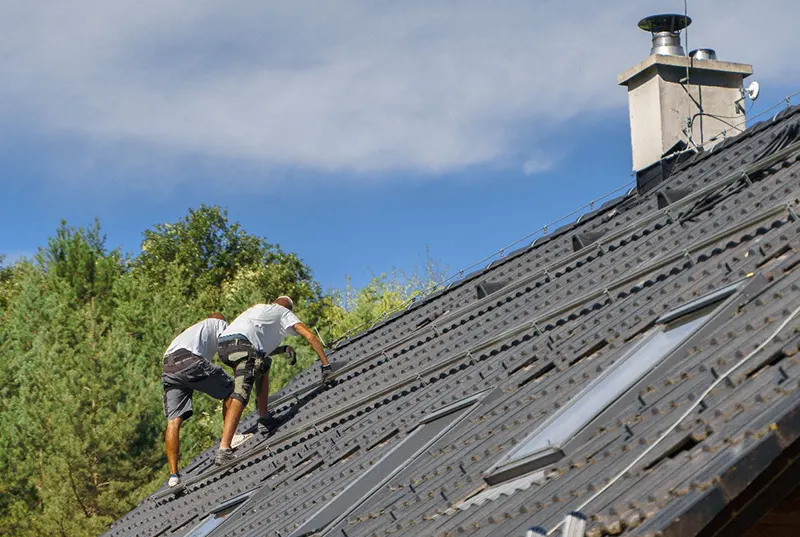 Two professional roofing contractors from a Central Florida roofing company performing a roof replacement on a residential home under a clear blue sky, showcasing durable and high-quality roofing solutions.