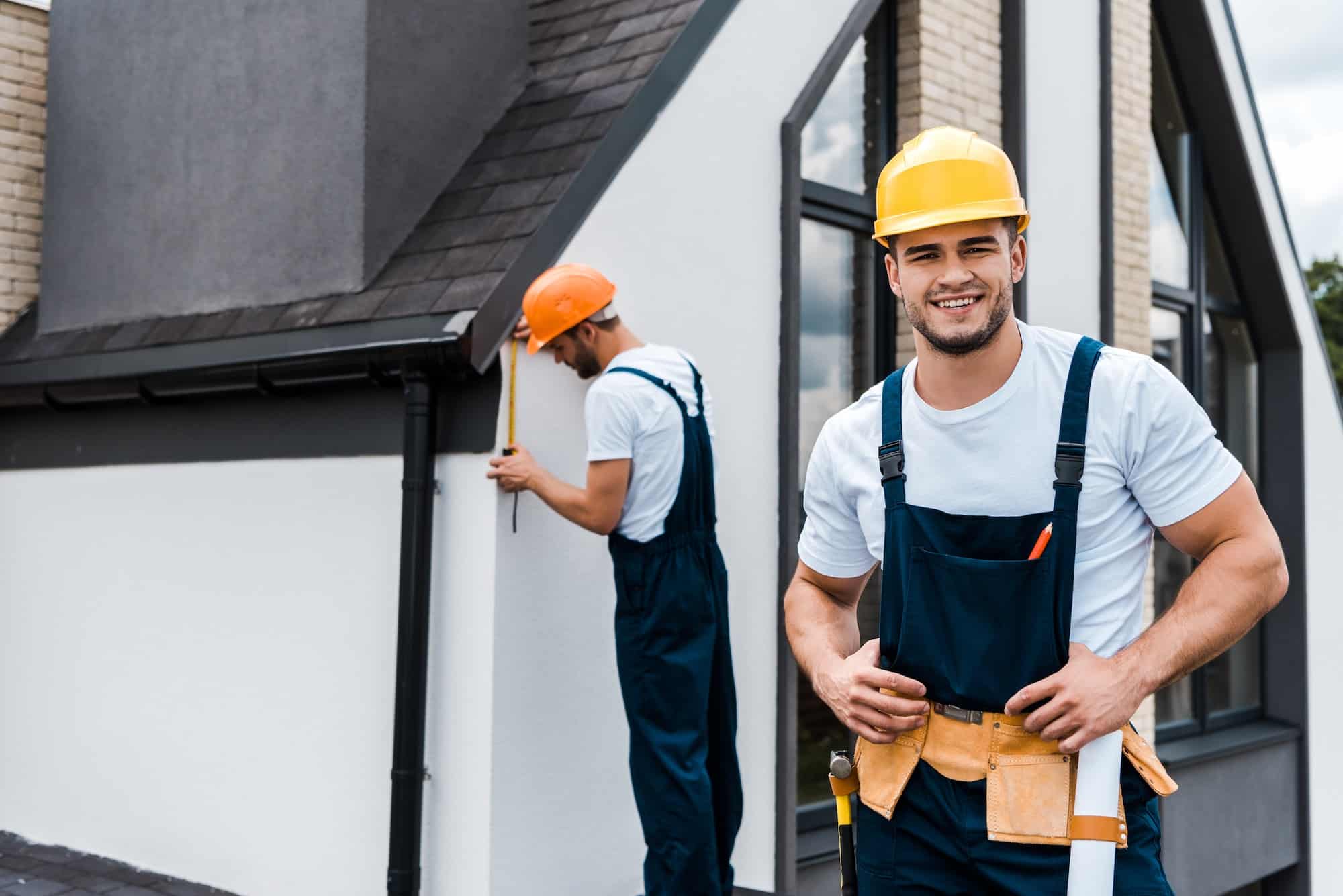 Two professional roofing contractors from a Central Florida roofing company working on a residential roofing project. One contractor is inspecting the gutter while the other smiles confidently, representing expertise in residential and commercial roofing services.