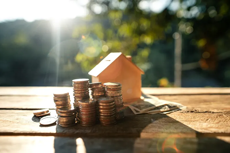 Stacks of coins and a small house model on a wooden table, symbolizing affordable financing options provided by a Central Florida roofing company to help homeowners with roofing projects