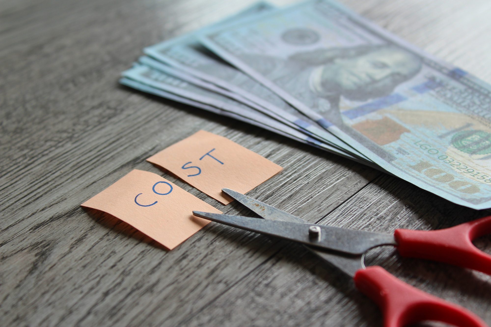 Scissors cutting a note with the word "COST," symbolizing the long-term savings and value of Architectural Shingles due to their durability and energy efficiency.
