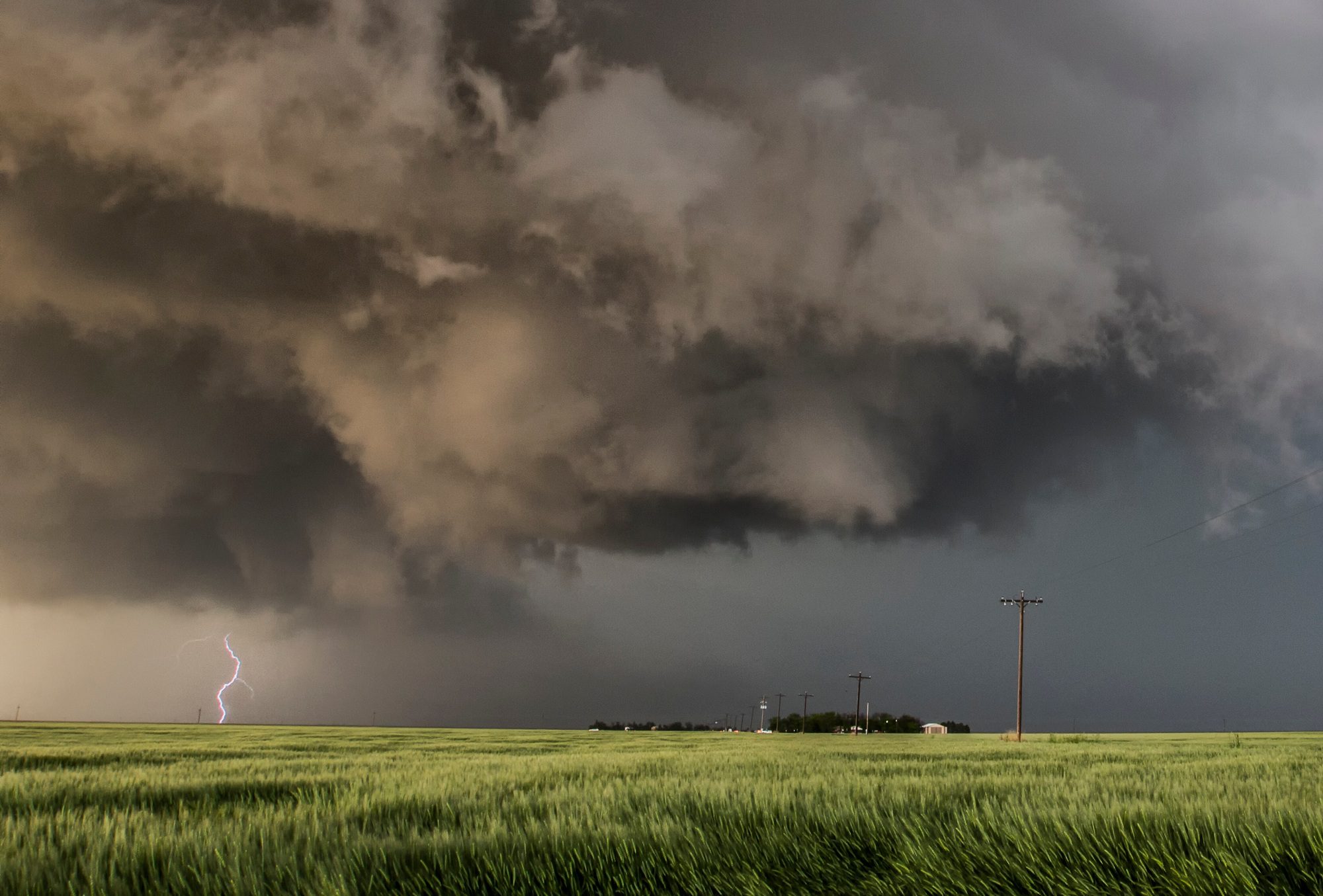 Dark storm clouds loom over a green field as lightning strikes, symbolizing severe weather challenges. Orlando roofing problems often arise from intense storms, making timely inspections and repairs essential for home protection.